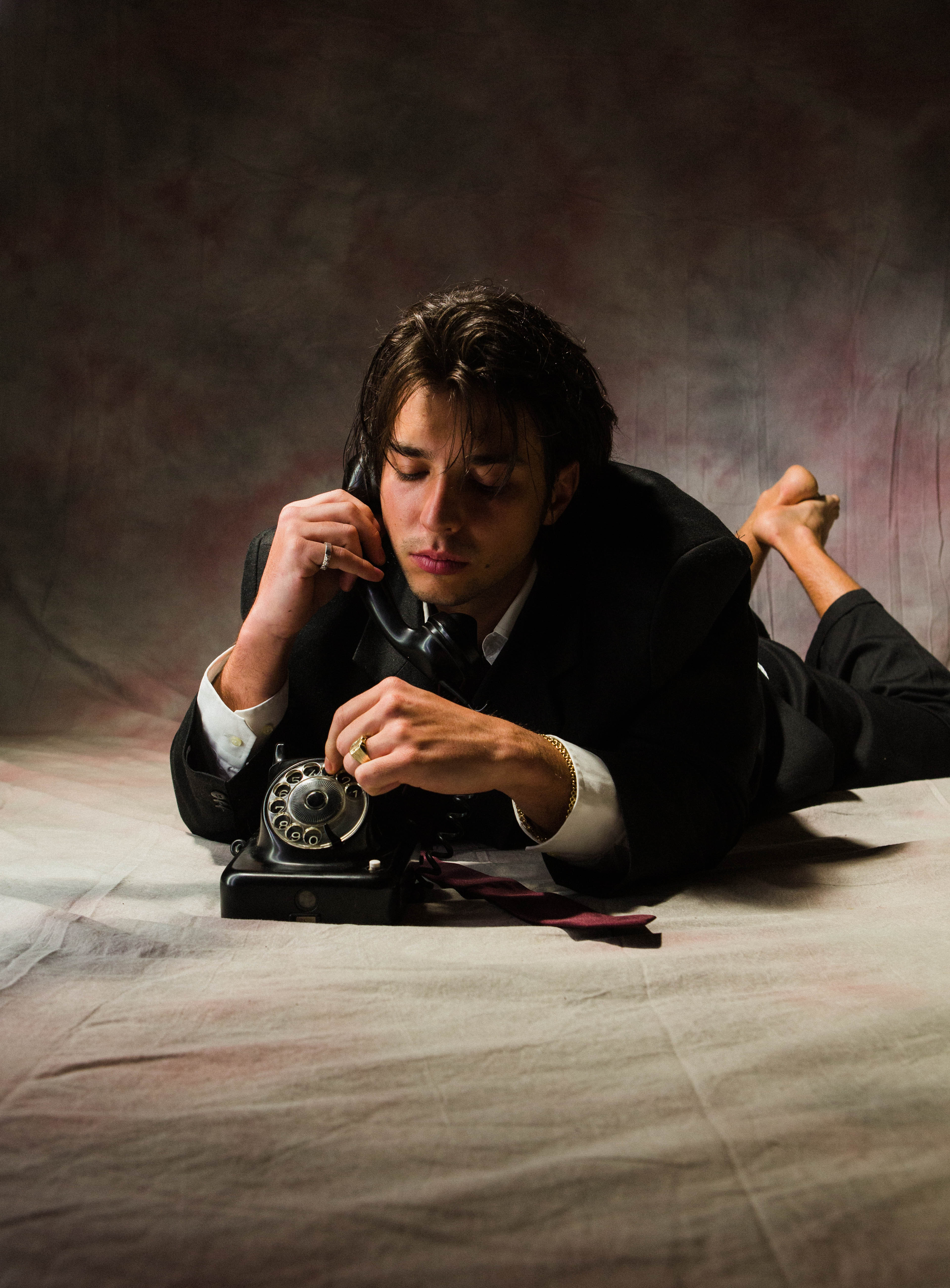 Das Bild zeigt den Musiker Bibiza, wie er in einem schwarzen Anzug auf dem Bauch liegend mit einem alten Wählscheibentelefon telefoniert.