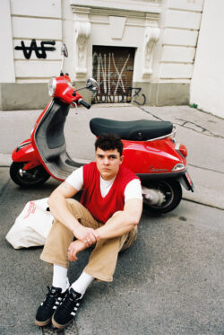 Das Foto zeigt den Künstler Kilean812 vor einem roten Motorroller auf dem Boden sitzend.